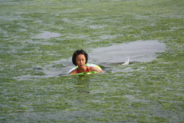A girl swims at a bathing beach filled with green algae in Eash China's coastal city Qingdao, July 16, 2011. [Photo/Xinhua] 