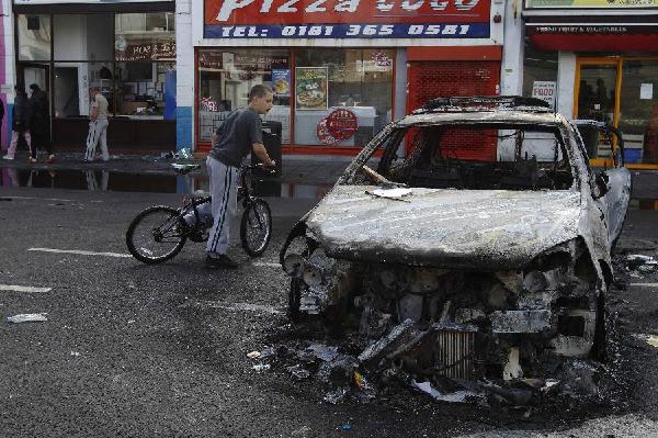 A child looks into the remains of a police car set alight and burned during riots in Tottenham, north London, August 7, 2011. [Xinhua]