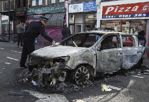 A police officer removes identification from a police car set alight and burned during riots in Tottenham, north London, August 7, 2011. Rioters throwing petrol bombs battled police in a economically deprived district of London overnight, setting patrol cars, buildings and a double-decker bus on fire in some of the worst disorder seen in the capital for recent years. [Xinhua]