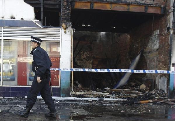 A police officer cordons off shops set alight and burned during riots in Tottenham, north London, August 7, 2011. Rioters throwing petrol bombs battled police in a economically deprived district of London overnight, setting patrol cars, buildings and a double-decker bus on fire in some of the worst disorder seen in the capital for recent years. [Xinhua]